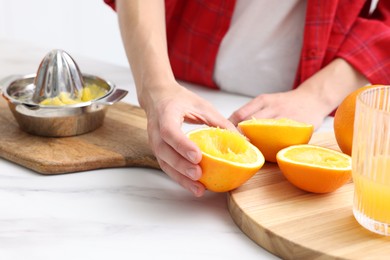 Photo of Making juice. Woman with squeezed orange at white marble table indoors, closeup