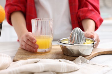 Photo of Woman with freshly squeezed orange juice and juicer at table indoors, closeup