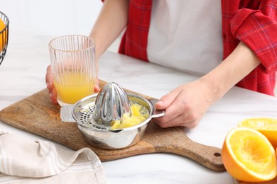 Photo of Woman with freshly squeezed orange juice and juicer at white marble table indoors, closeup