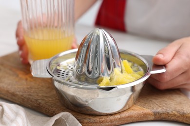 Photo of Woman with freshly squeezed orange juice and juicer at table indoors, closeup