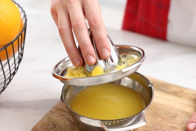 Photo of Woman with juicer and freshly squeezed orange juice at white marble table indoors, closeup