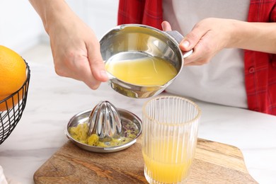 Photo of Woman pouring freshly squeezed orange juice into glass at white marble table indoors, closeup