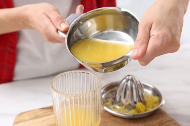 Photo of Woman pouring freshly squeezed orange juice into glass at white marble table indoors, closeup