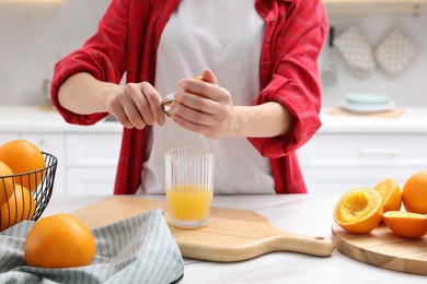 Photo of Making juice. Woman with orange using juicer at white marble table indoors, closeup