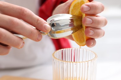 Photo of Making juice. Woman with orange using juicer indoors, closeup
