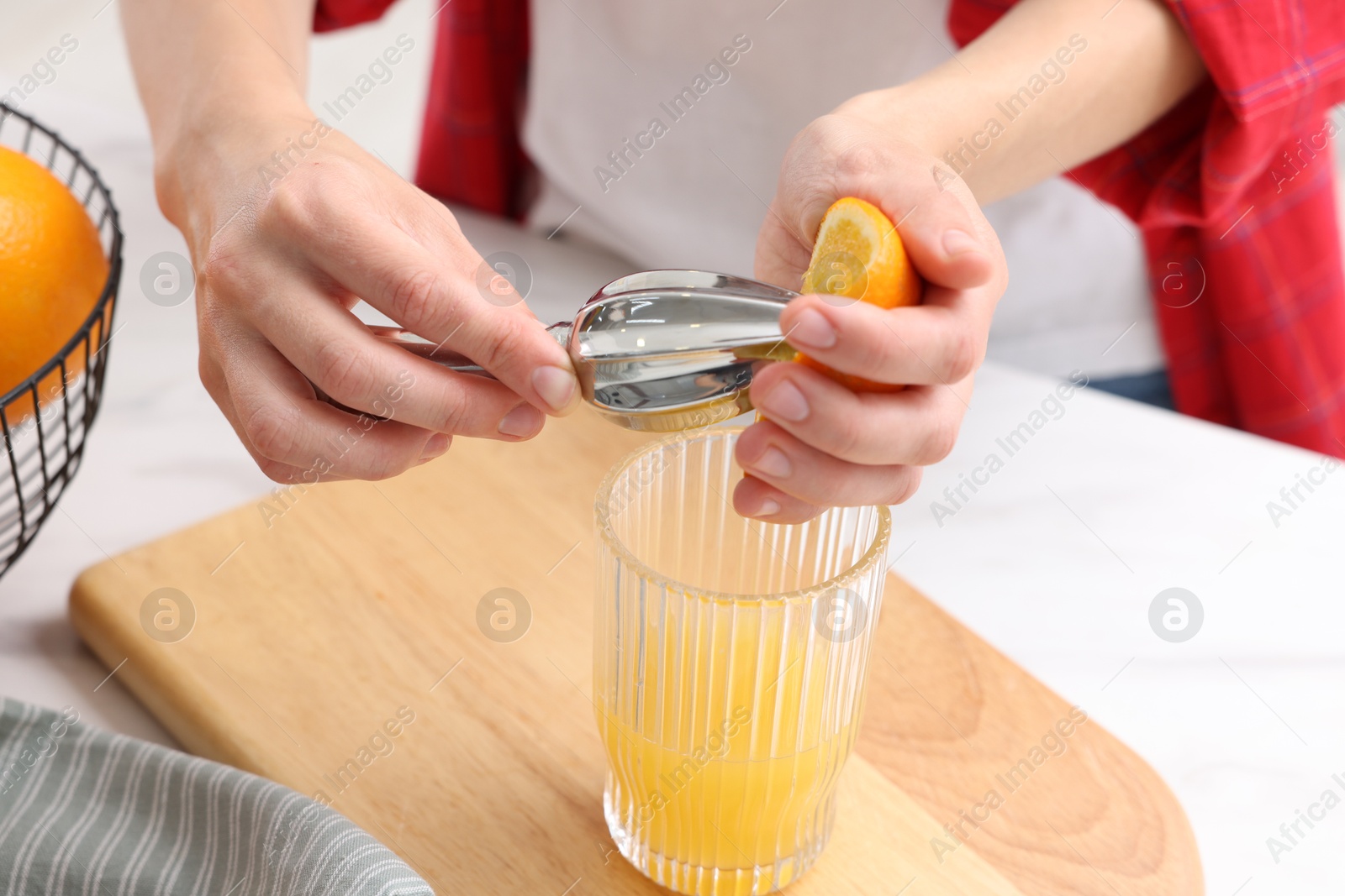 Making juice. Woman with orange using juicer at white marble table indoors, closeup Photo of Making juice. Woman with orange using juicer at white marble table indoors, closeup