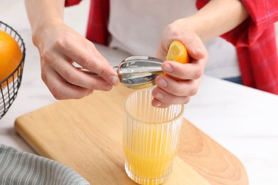 Photo of Making juice. Woman with orange using juicer at white marble table indoors, closeup