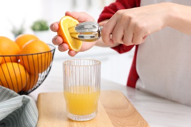 Photo of Making juice. Woman with orange using juicer at white marble table indoors, closeup
