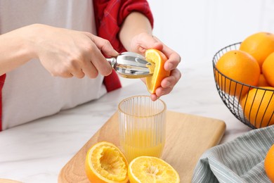 Photo of Making juice. Woman with orange using juicer at white marble table indoors, closeup