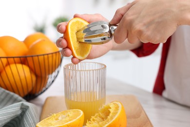 Photo of Making juice. Woman with orange using juicer at table indoors, closeup