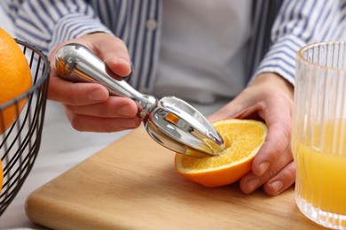 Photo of Making juice. Woman with orange using juicer at table indoors, closeup