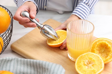 Photo of Making juice. Woman with orange using juicer at white marble table indoors, closeup