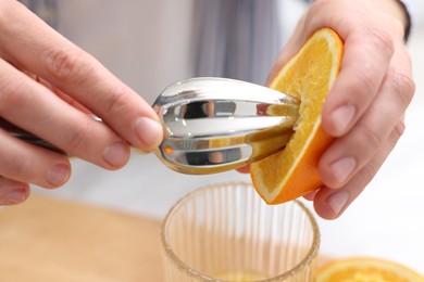 Photo of Making juice. Woman with orange using juicer at table indoors, closeup
