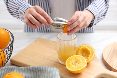 Photo of Making juice. Woman with orange using juicer at white marble table indoors, closeup