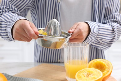 Photo of Woman pouring freshly squeezed orange juice into glass at table indoors, closeup