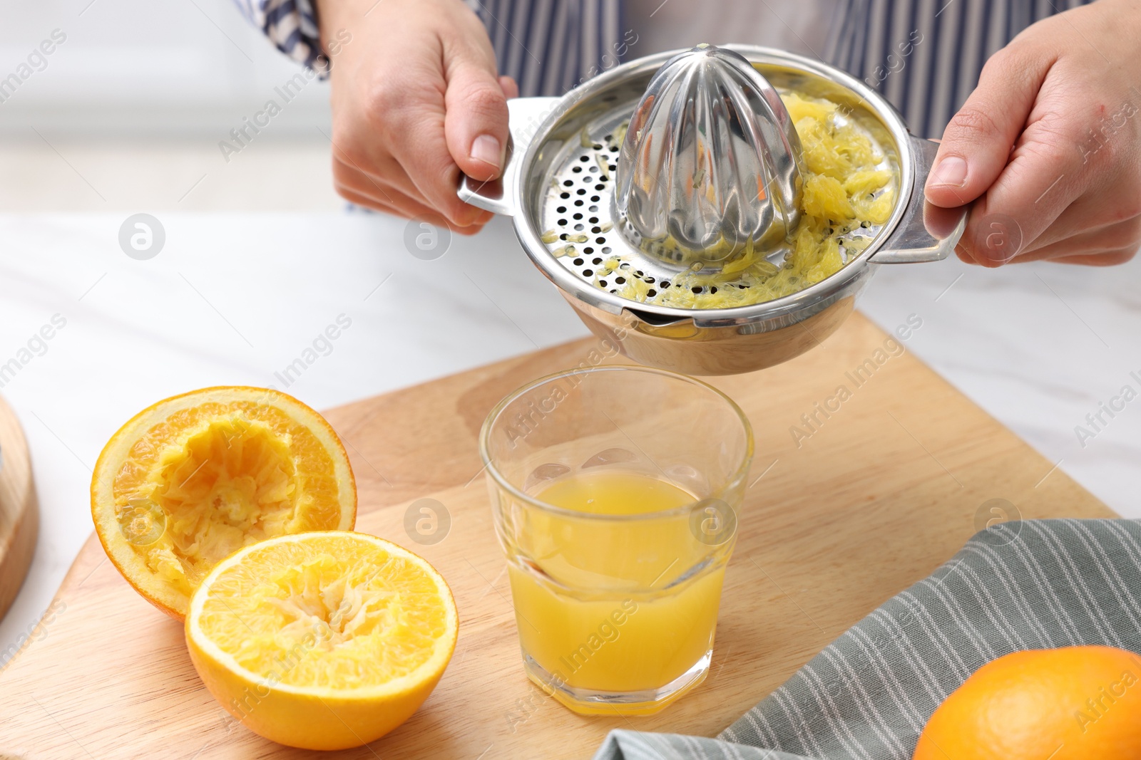 Woman pouring freshly squeezed orange juice into glass at white marble table indoors, closeup Photo of Woman pouring freshly squeezed orange juice into glass at white marble table indoors, closeup