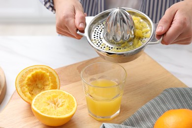 Photo of Woman pouring freshly squeezed orange juice into glass at white marble table indoors, closeup