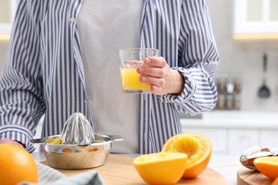 Photo of Woman with glass of freshly squeezed orange juice at table indoors, closeup
