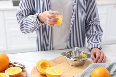 Photo of Woman with glass of freshly squeezed orange juice at white marble table indoors, closeup