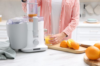 Photo of Woman making fresh orange juice with modern juicer at white marble table indoors, closeup