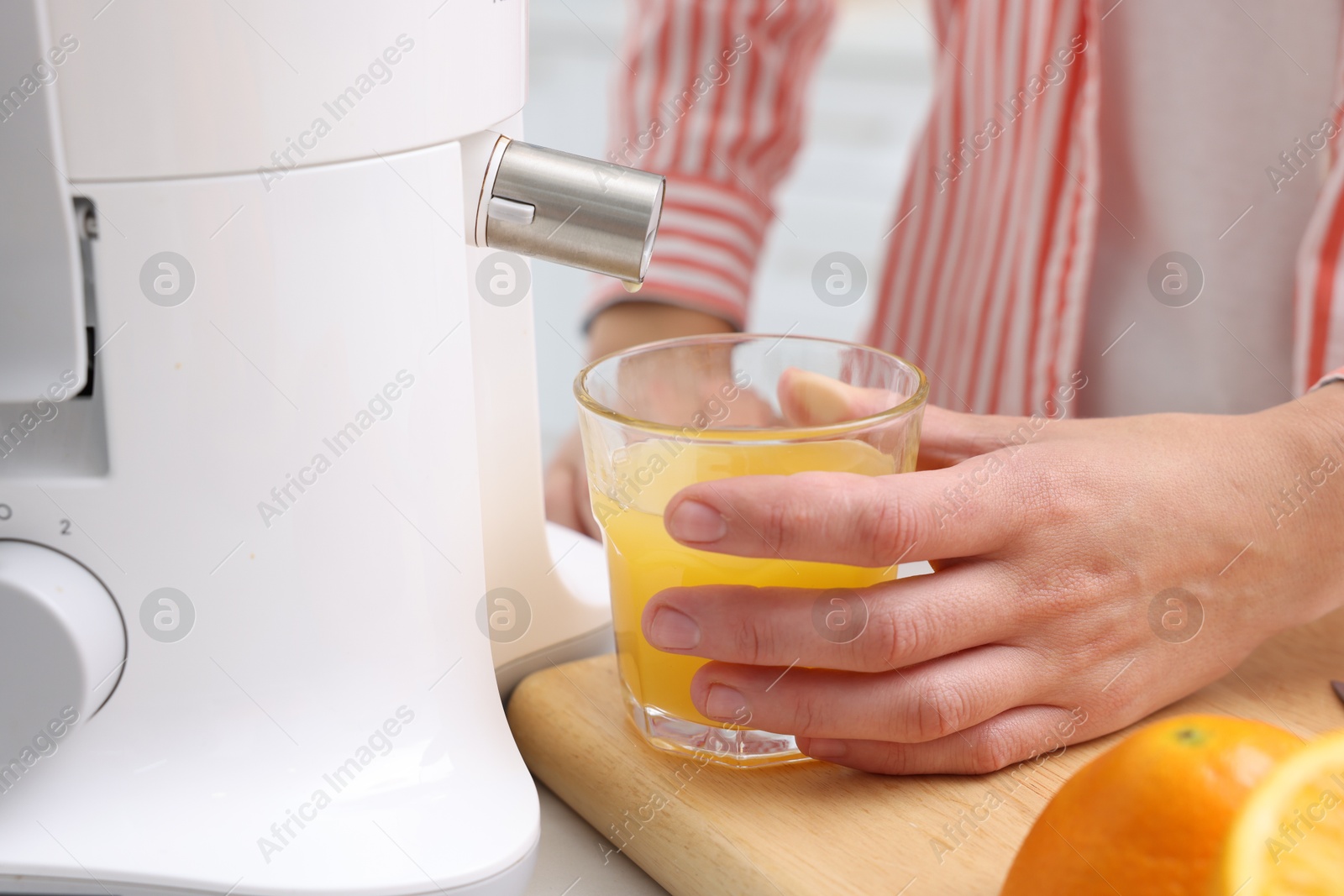 Photo of Woman making fresh orange juice with modern juicer at table indoors, closeup