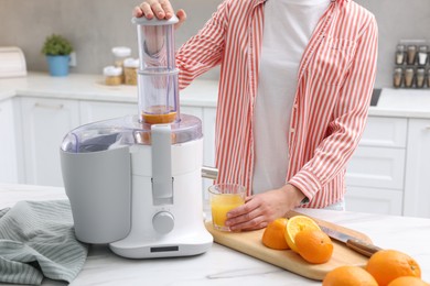 Photo of Woman making fresh orange juice with modern juicer at white marble table indoors, closeup