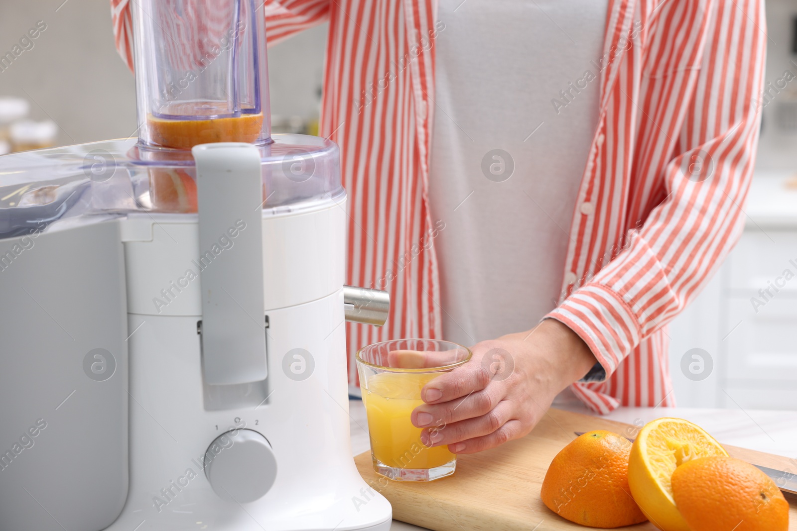 Woman making fresh orange juice with modern juicer at table indoors, closeup Photo of Woman making fresh orange juice with modern juicer at table indoors, closeup