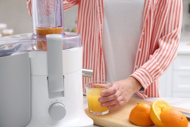 Photo of Woman making fresh orange juice with modern juicer at table indoors, closeup