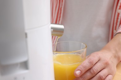 Photo of Woman making fresh orange juice with modern juicer indoors, closeup