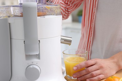 Photo of Woman making fresh orange juice with modern juicer indoors, closeup