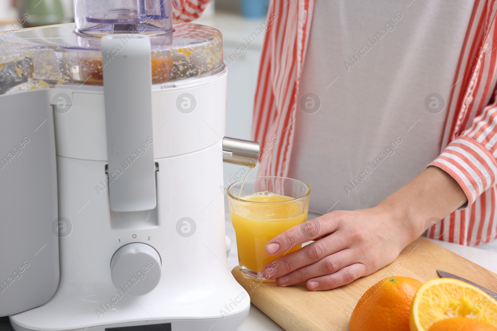 Photo of Woman making fresh orange juice with modern juicer at table indoors, closeup
