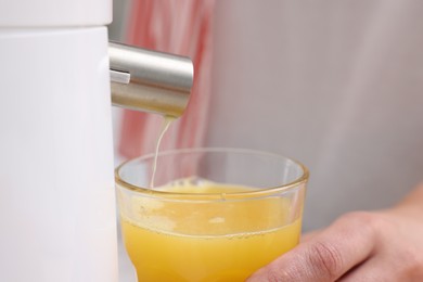 Photo of Woman making fresh orange juice with modern juicer indoors, closeup