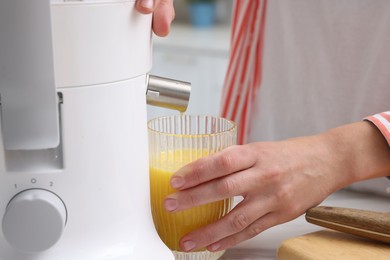 Photo of Woman making fresh orange juice with modern juicer at table indoors, closeup