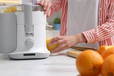 Photo of Woman making fresh orange juice with modern juicer at white marble table indoors, closeup
