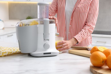 Photo of Woman making fresh orange juice with modern juicer at white marble table indoors, closeup