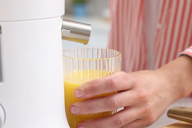 Photo of Woman making fresh orange juice with modern juicer indoors, closeup