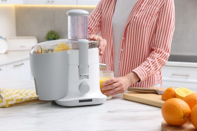 Photo of Woman making fresh orange juice with modern juicer at white marble table indoors, closeup