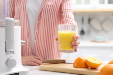 Photo of Woman with glass of freshly squeezed orange juice at table indoors, closeup