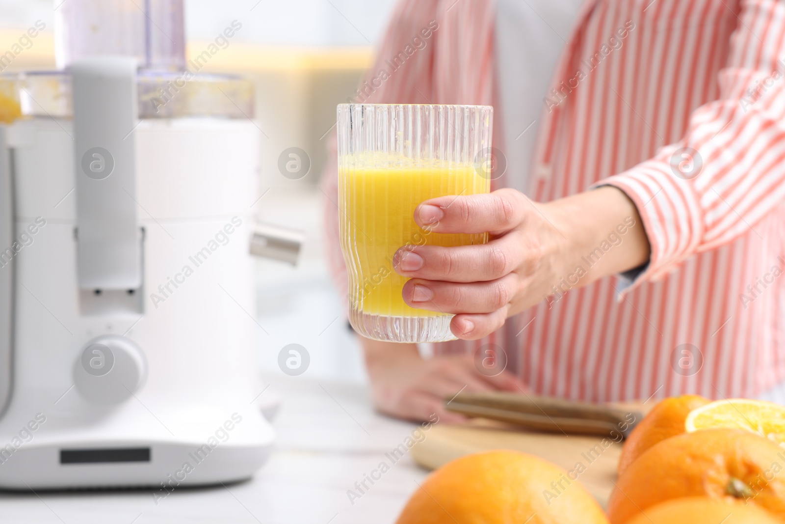 Woman with glass of freshly squeezed orange juice at table indoors, closeup Photo of Woman with glass of freshly squeezed orange juice at table indoors, closeup