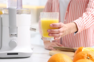 Photo of Woman with glass of freshly squeezed orange juice at table indoors, closeup