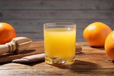 Photo of Freshly squeezed orange juice, fruits and juicer on wooden table, closeup