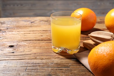 Photo of Freshly squeezed orange juice, fruits and juicer on wooden table, closeup. Space for text