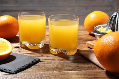 Photo of Freshly squeezed orange juice, fruits and juicer on wooden table, closeup