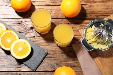 Photo of Freshly squeezed orange juice, fruits and juicer on wooden table, flat lay