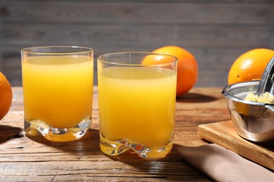 Photo of Freshly squeezed orange juice, fruits and juicer on wooden table, closeup