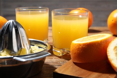 Photo of Freshly squeezed orange juice, fruits and juicer on wooden table, closeup