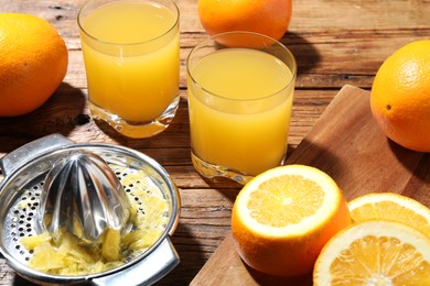 Photo of Freshly squeezed orange juice, fruits and juicer on wooden table, closeup