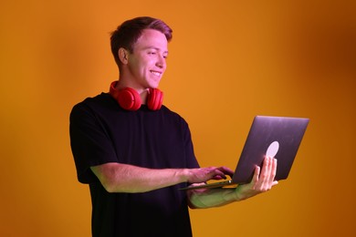 Photo of Smiling man with headphones using laptop in neon lights against orange background