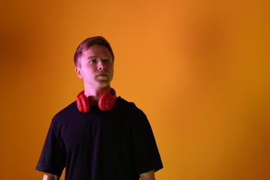 Photo of Handsome man with headphones in neon lights against orange background. Space for text
