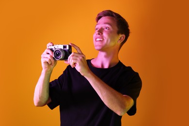 Photo of Smiling man with camera taking photo in neon lights against orange background